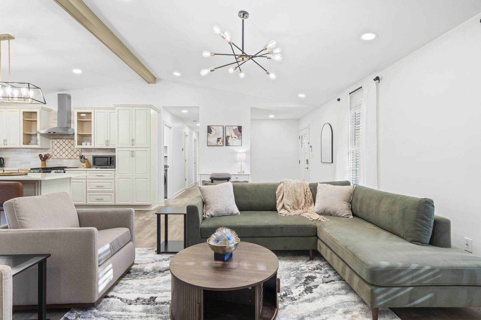 An open living room and kitchen in a furnished home, with a sectional sofa and a round coffee table